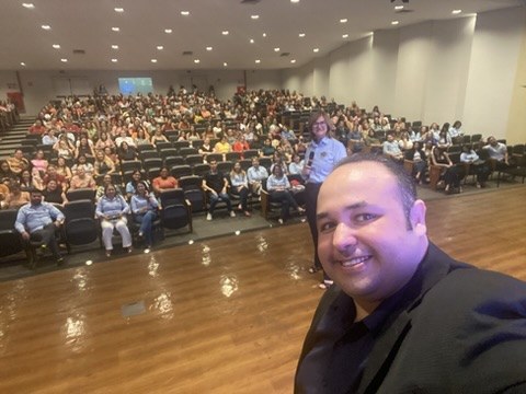 Renan Sargiani ao lado de um auditório repleto de participantes ao fim de uma palestra